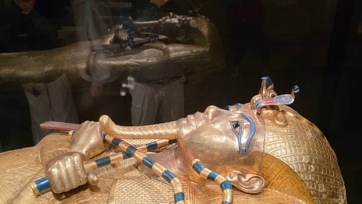 Close-up of the golden sarcophagus mask of Tutankhamun displayed behind glass