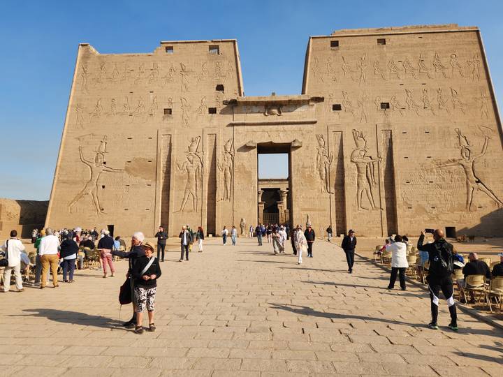 Crowds entering the monumental pylon entrance of Edfu Temple adorned with hieroglyphic reliefs