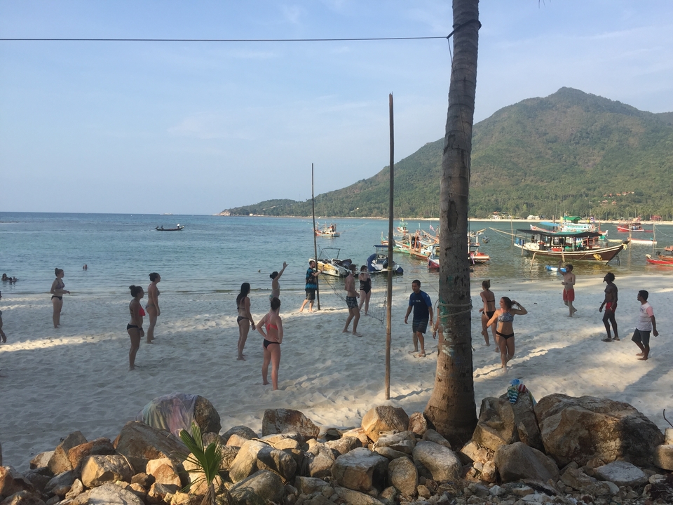 People playing volleyball on a beach surrounded by boats and hills.