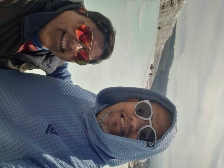 Couple takes a selfie with the pale turquoise thermal pools of Pamukkale behind them.