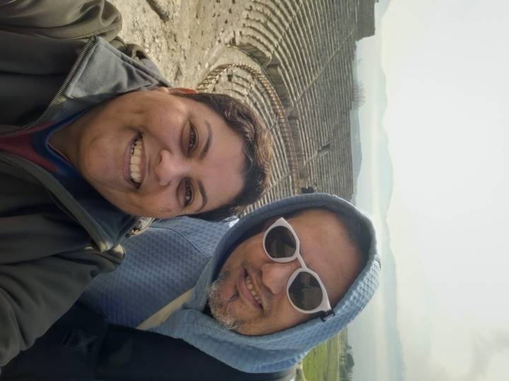 Smiling couple selfie overlooking the stone tiers of an ancient amphitheatre.