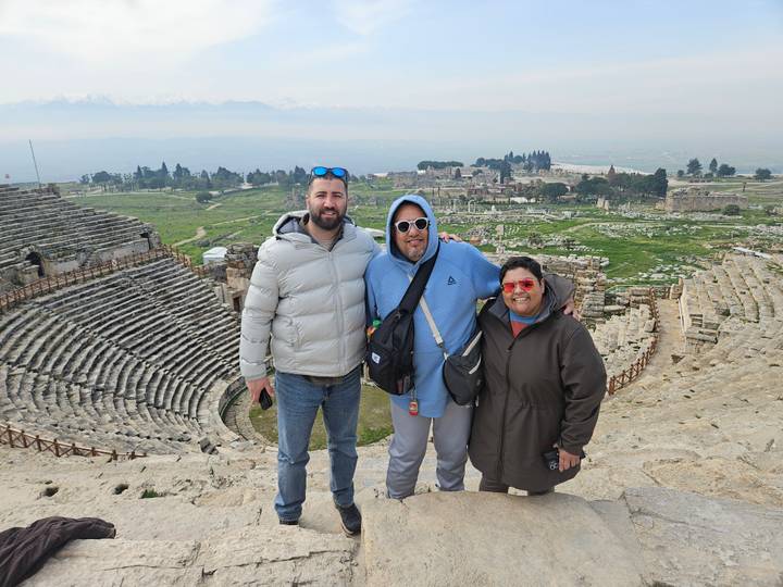 Three travellers pose at the top of Hierapolis theatre with sprawling ruins below.