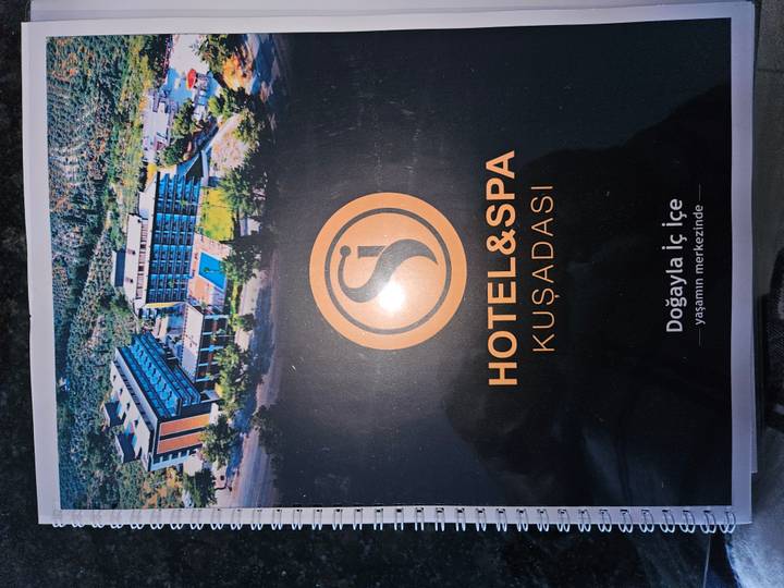 Promotional graphic showing an aerial photo of a seaside hotel & spa in Kuşadası with brand logo.