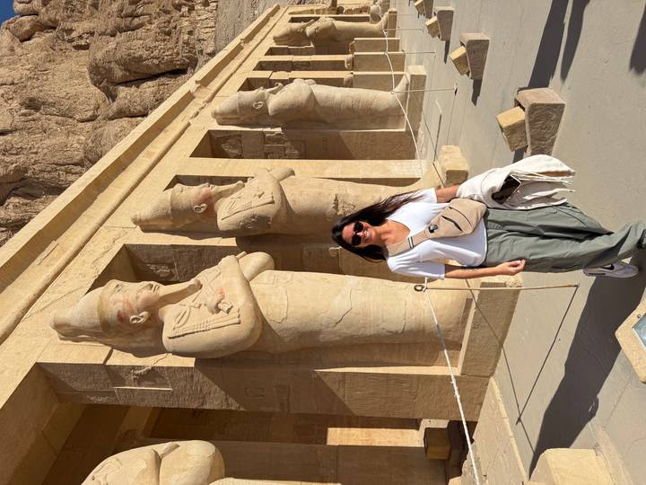 Female traveller stands in front of massive sandstone statues carved into an Egyptian temple facade.