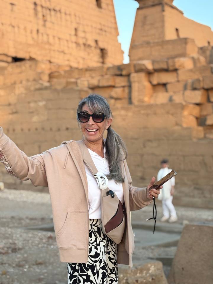 Cheerful woman poses with ancient sandstone ruins softly glowing in evening light.