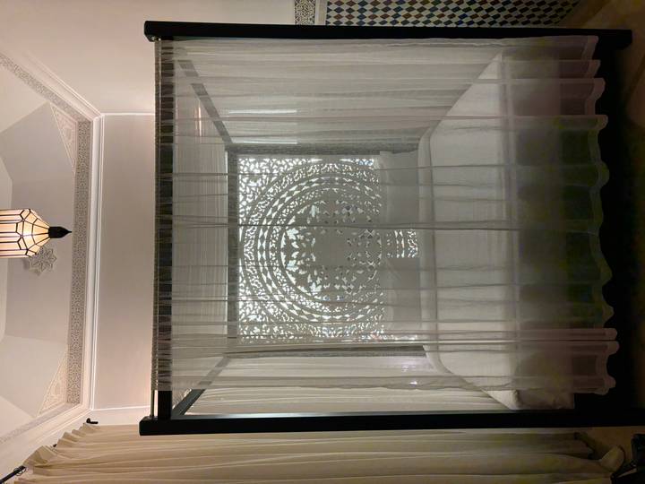 Elegant four-poster bed behind sheer curtains with intricate latticework backdrop.