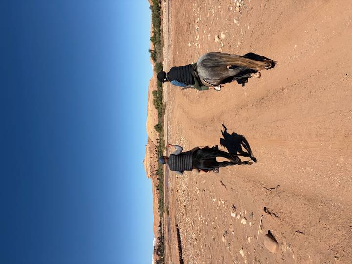 Two riders on horseback follow a dusty track toward a desert kasbah.