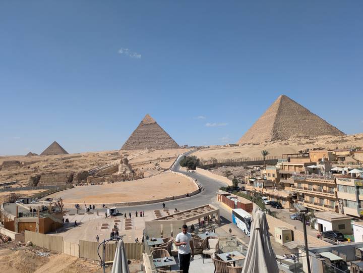 Iconic Great Pyramids of Giza rise above desert sands under clear blue sky with scattered visitors below.