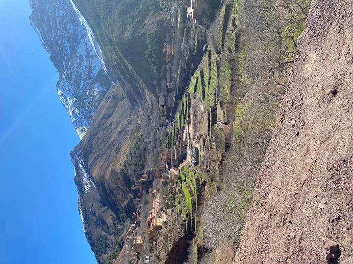 Green valley villages and terraced fields beneath rugged snowy Atlas peaks.