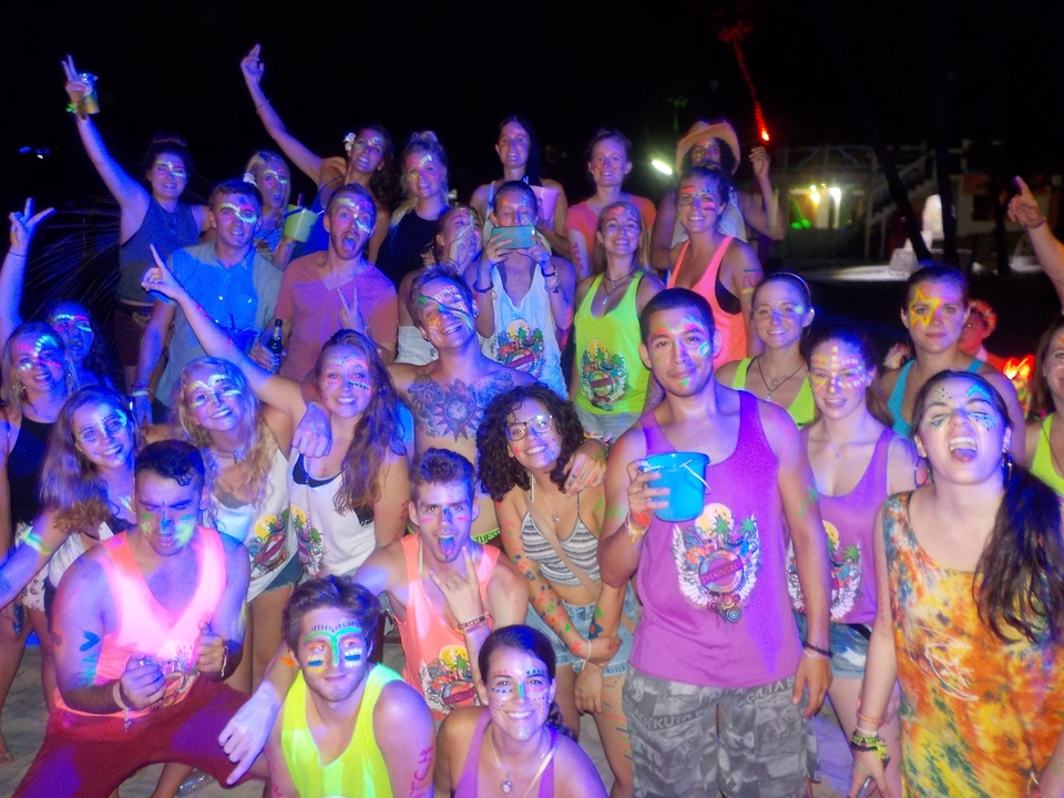 Group of people having a party outside, with colorful face paint and drinks.