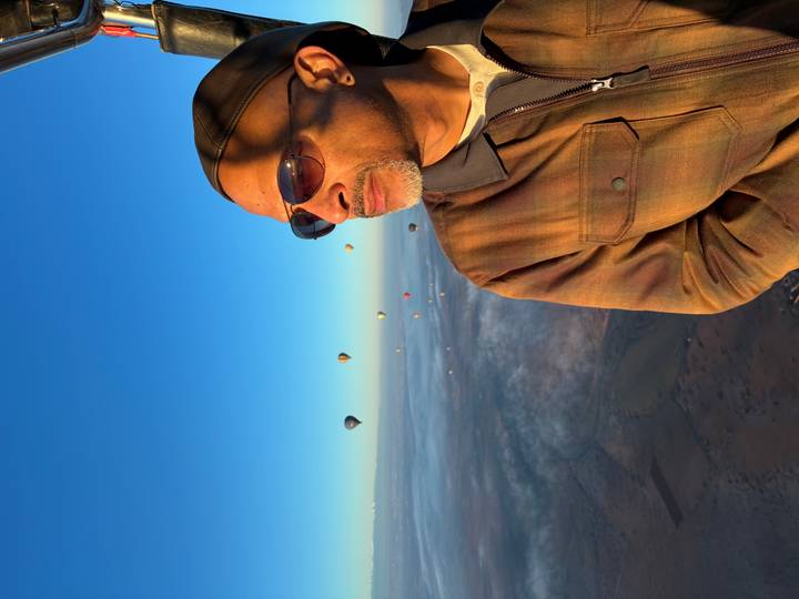 Man wearing sunglasses enjoying hot-air balloon ride high above morning clouds.