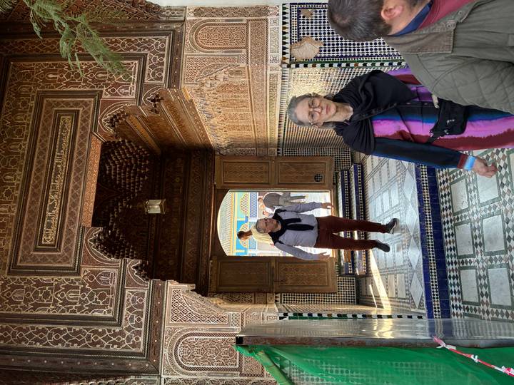 Visitors walking through ornate tiled archway of a Moroccan palace.