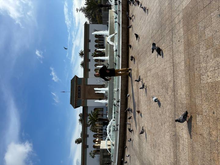 Man among pigeons in front of fountain and colonial building in Casablanca square.