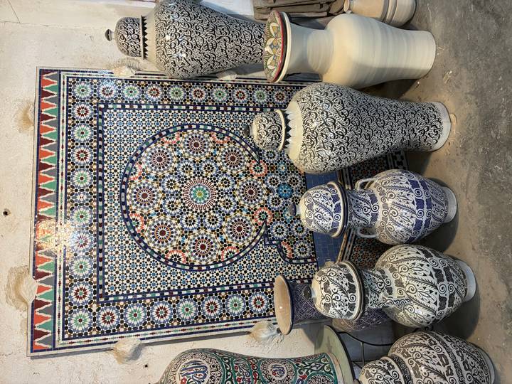 Display of traditional blue-and-white Moroccan pottery in front of a colourful zellige mosaic panel inside a workshop