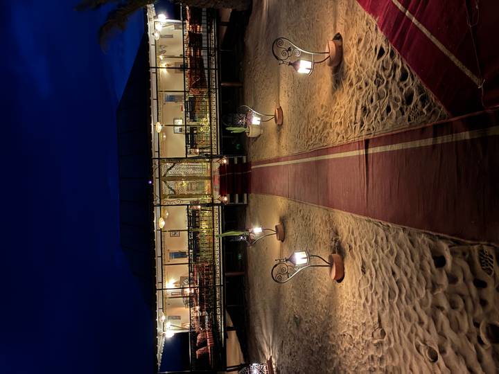 Nighttime view of a luxury desert camp with illuminated pathway lamps leading to a canvas dining tent on sandy terrain