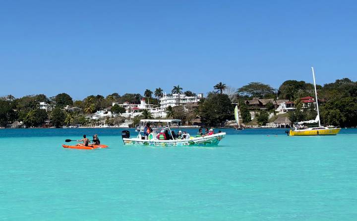 Kayaks and small tour boats float on the brilliant turquoise waters of Bacalar Lagoon with villas and palms in the distance.