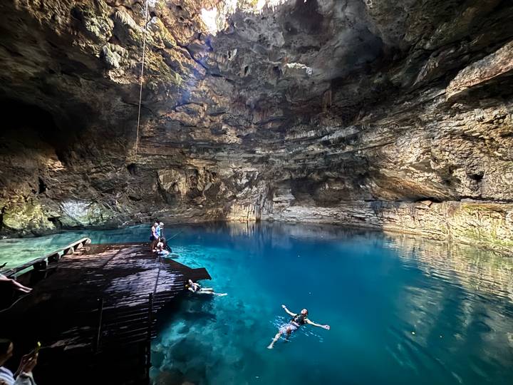 Visitors swim and relax in the crystal-clear blue waters of a dramatic underground cenote.