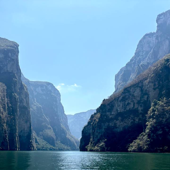 Towering limestone walls of a steep canyon frame a bright blue sky.