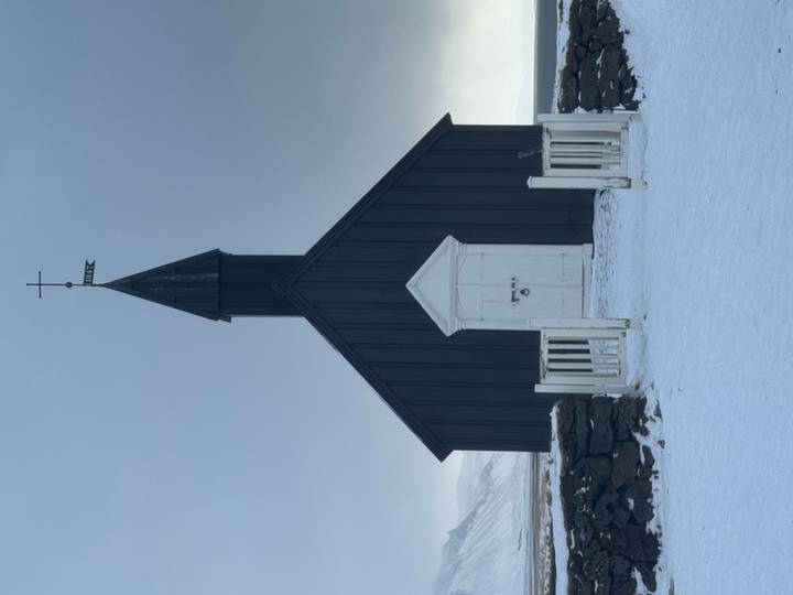 Iconic black wooden church with simple white gate set against a snowy Icelandic landscape.