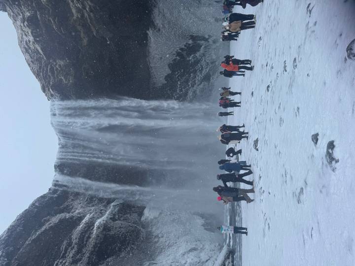 Visitors wearing winter gear stand before a powerful waterfall cascading into a snowy basin.