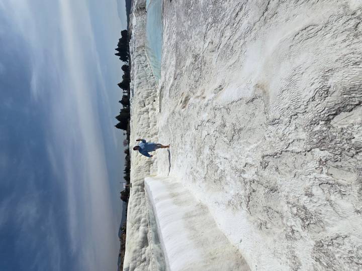 Person joyfully walks barefoot along the dazzling white travertine terraces of Pamukkale beside turquoise pools.