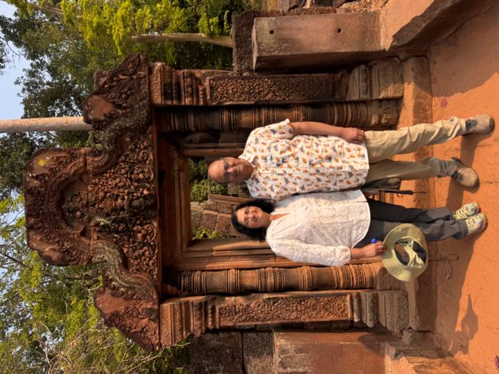 Couple standing in an ornate red-sandstone doorway richly carved at Banteay Srei temple.