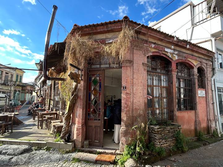 Weathered pink stone café building with stained-glass door and rustic outdoor seating on a narrow Turkish street.