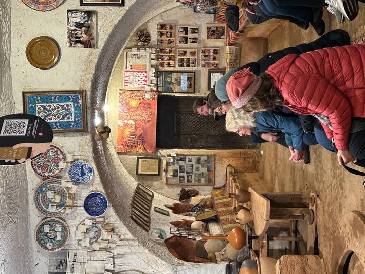 Visitors seated inside a pottery studio adorned with decorated plates and photos as a host demonstrates craft.