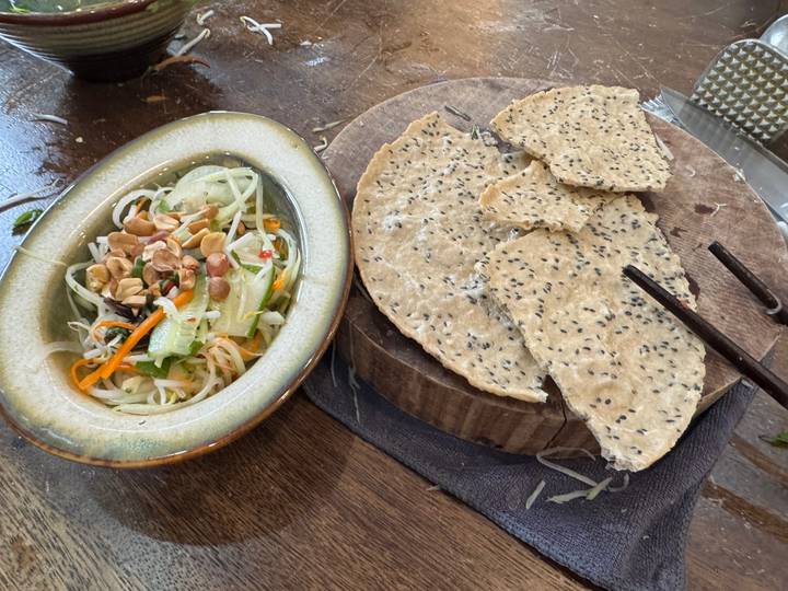 Overhead view of fresh salad with chopped peanuts and broken sesame crackers on a wooden board.