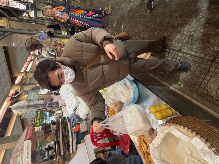 Masked shopper carrying a bag of groceries inside a busy indoor market aisle.