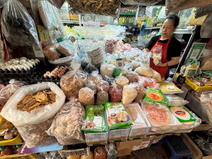 Indoor market stall stacked high with dried goods, grains, noodles and eggs in plastic bags.