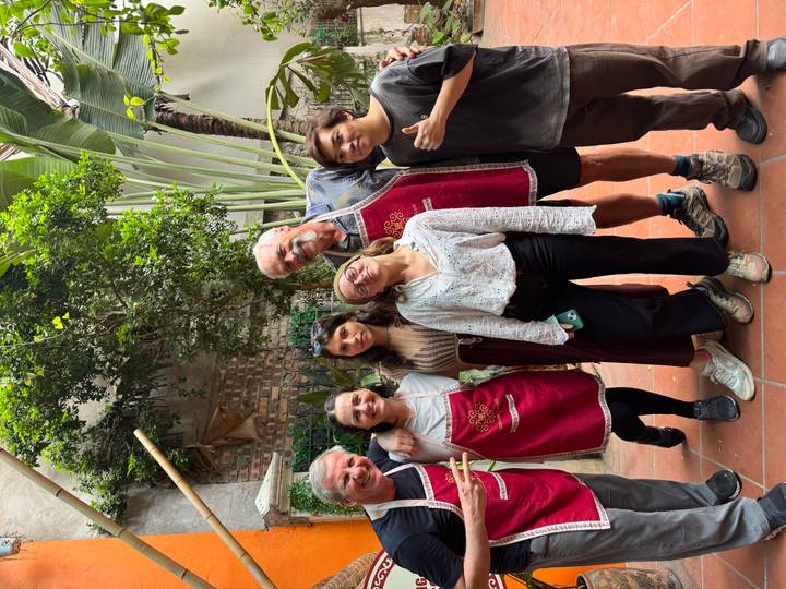 Smiling participants wearing red aprons posing together in a courtyard after a cooking class.