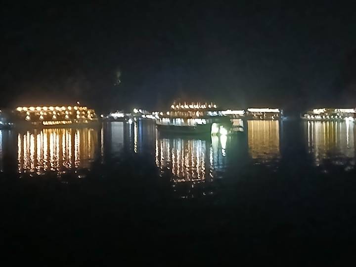 Nighttime view of blurry illuminated boats reflecting orange lights on dark water.