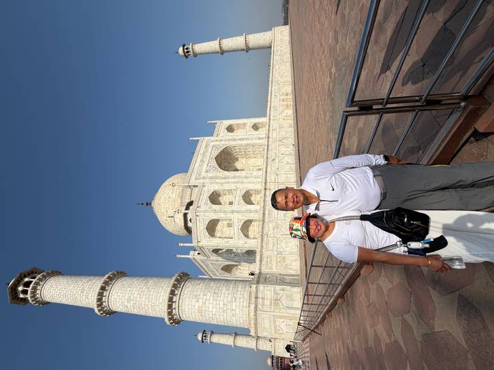 Couple smiling beside a Taj Mahal minaret under a deep blue sky.