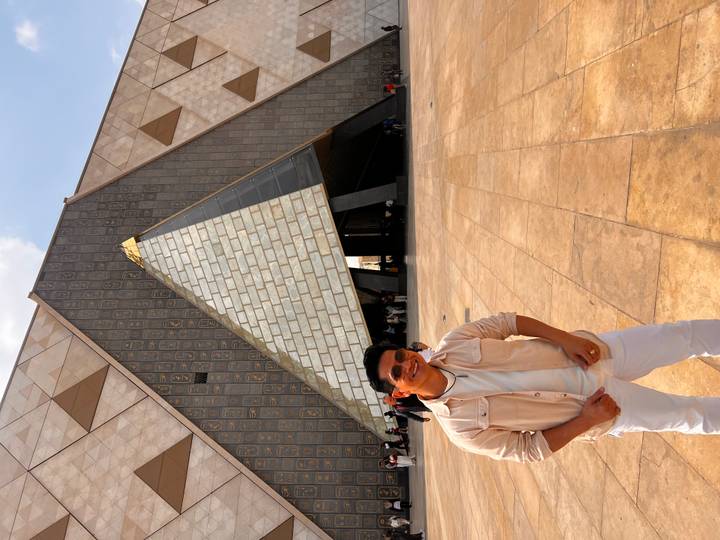 Visitor stands outside the striking triangular entrance of the Grand Egyptian Museum.