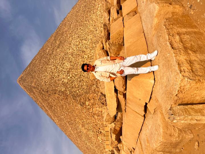 Traveller stands on large cut stones before the towering Great Pyramid.