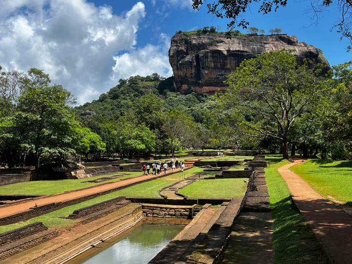 Visitors walk through landscaped ancient gardens below the towering Sigiriya Rock Fortress.