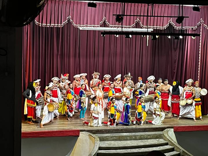 Traditional Kandyan dance troupe in vibrant costumes take a group bow on theatre stage.