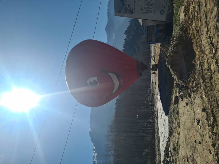 Red smiling hot-air balloon on a sunny morning with snowy peaks in the distance.