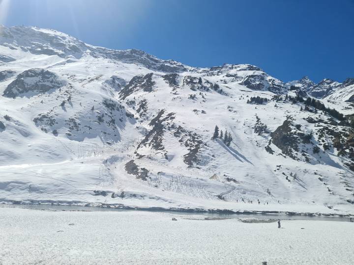 Expansive snowy mountain slope with jagged peaks and a frozen river under clear blue sky.