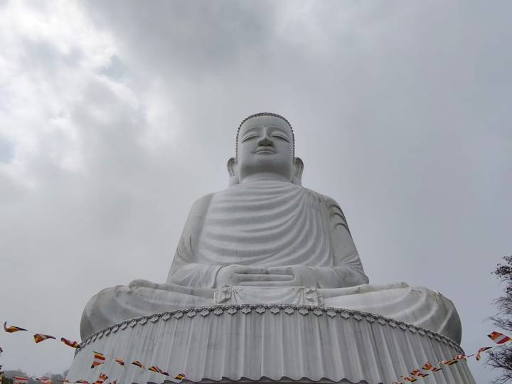 Large white seated Buddha statue rises against a cloudy sky.