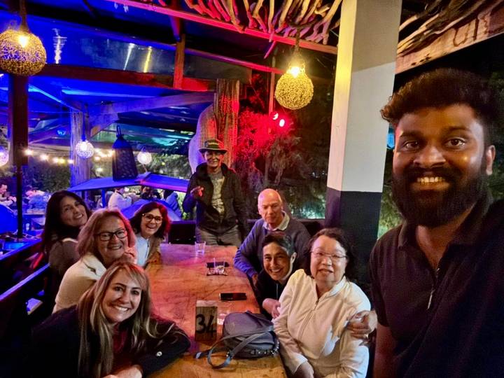 Friends enjoy drinks around a wooden table in a dimly lit bar with colourful lights.