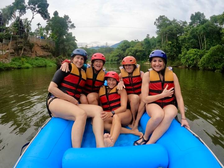 Women in life vests sit on an inflatable raft on a jungle river ready for rafting.