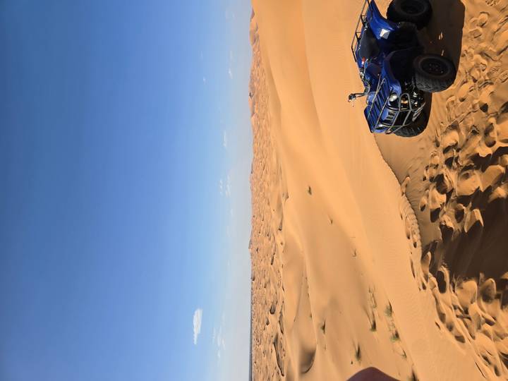 Golden sand dunes under a clear blue sky with part of a blue quad bike parked on the ridge.