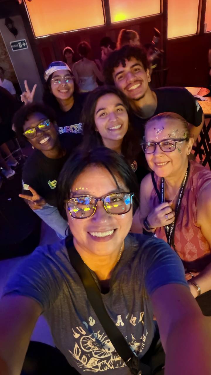 Close-up selfie of four friends with glitter face paint enjoying a festive indoor party.