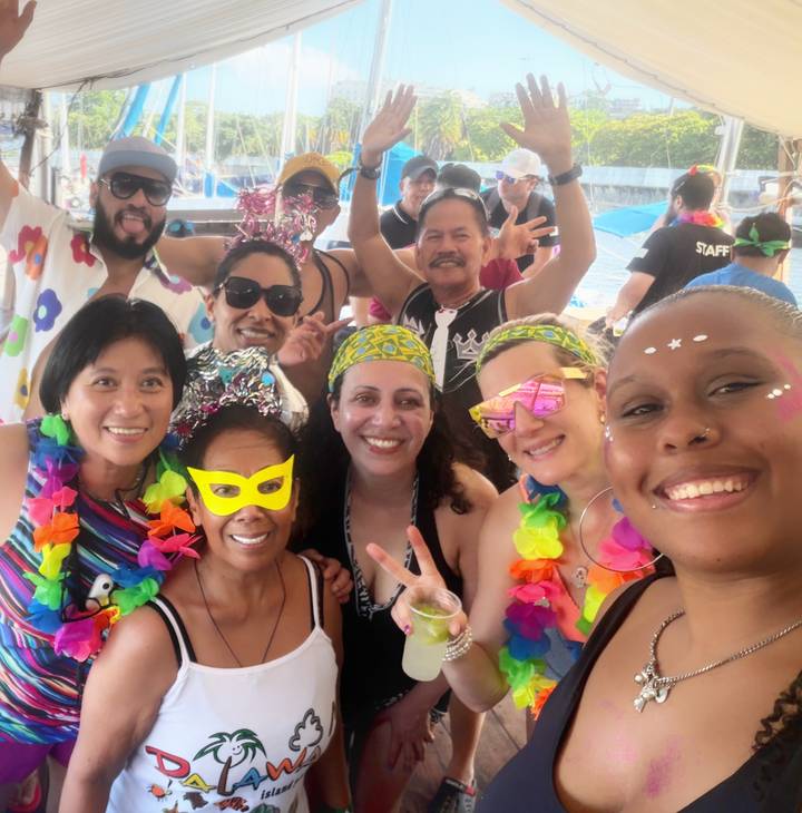 Smiling friends in colorful carnival costumes posing together at a lively pool party.