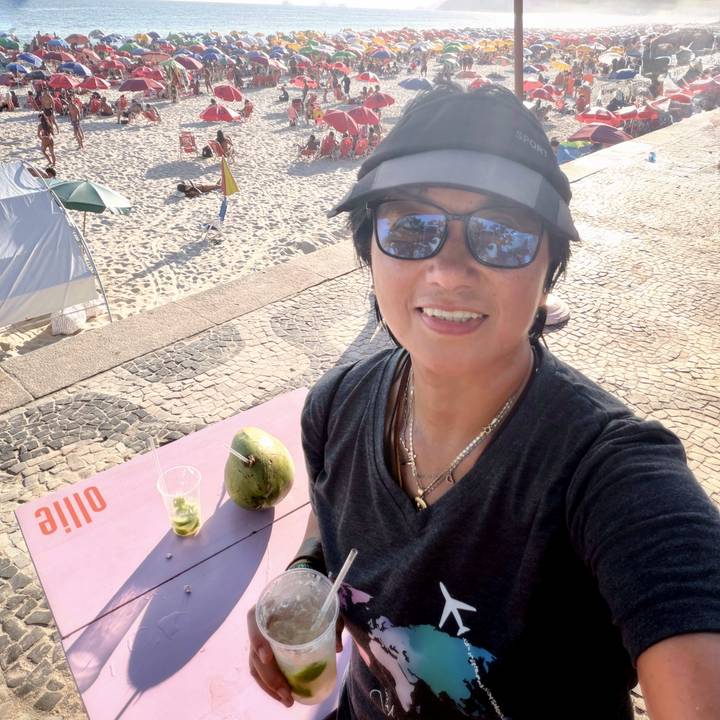 Woman taking a selfie on a beachfront promenade with a coconut drink on the table.