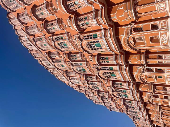 Upward angle of the ornate pink sandstone façade of Hawa Mahal against a vivid blue sky in Jaipur