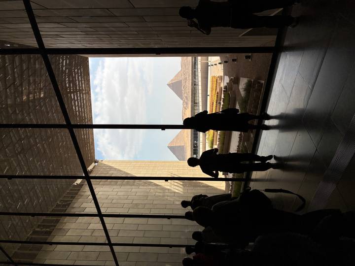 Museum visitors framed in silhouette look out huge glass wall at Giza pyramids in distance