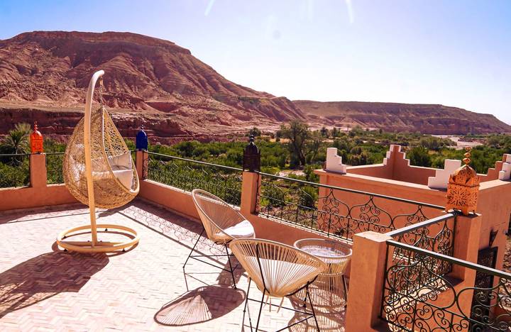 Scenic terrace of a riad with hanging chair overlooking red cliffs and oasis below